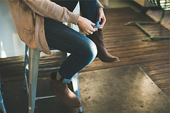 Woman putting on brown boots while sitting on stool