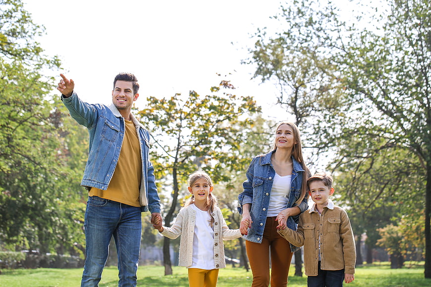 Happy family of four walking and pointing in a sunny park
