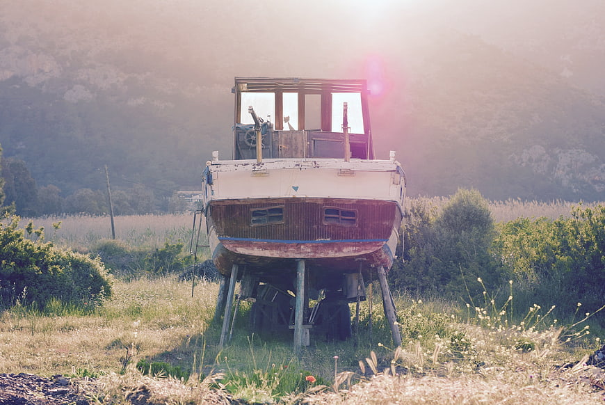 Old wooden boat on land in grassy field with sunset