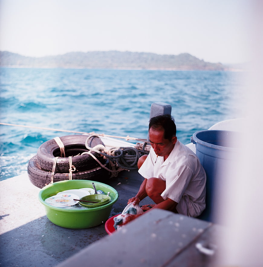 Man washing dishes on boat deck with ocean background