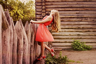 Woman in red dress leaning against rustic wooden fence