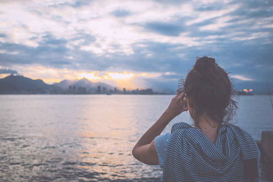 Woman on phone overlooking ocean sunset cityscape