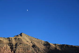 Crescent Moon Over Rocky Mountain Peak in Blue Sky