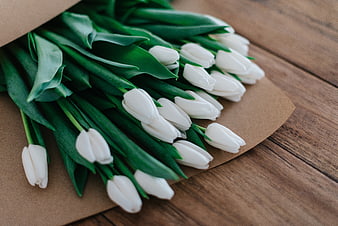 Bouquet of white tulips wrapped in brown paper on wood