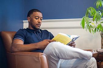 Young Black Man Reading Book in Leather Armchair