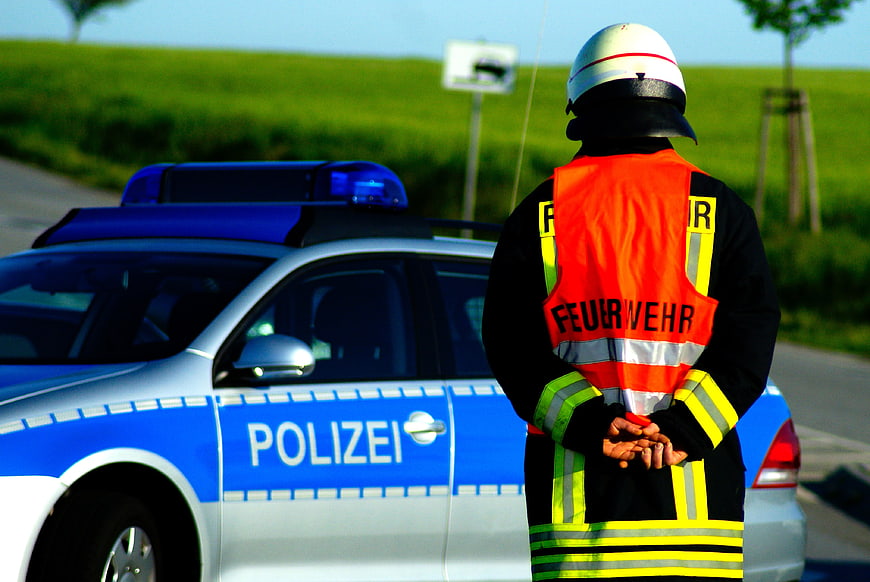 Firefighter in Safety Vest Standing Next to German Police Car