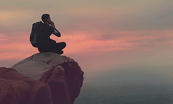 Man meditating on cliff edge at sunset with ocean view