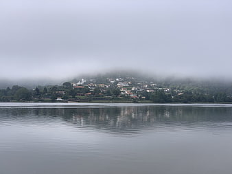 Misty lakeside village with foggy hills and water reflections