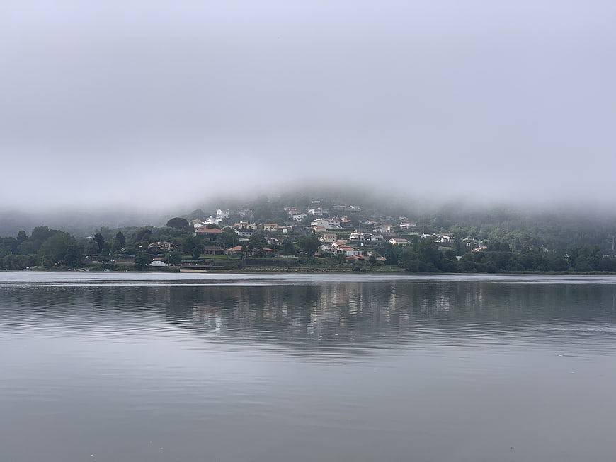 Misty lakeside village with foggy hills and water reflections