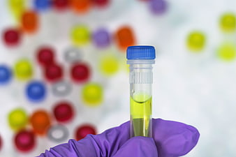 Gloved hand holding PCR tube with yellow liquid against blurred lab background