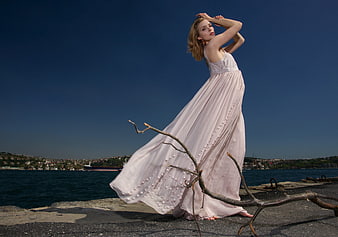 Young woman in flowing pink dress posing on coastal pier