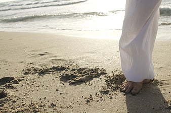 Bare feet in sand with white pants on a beach