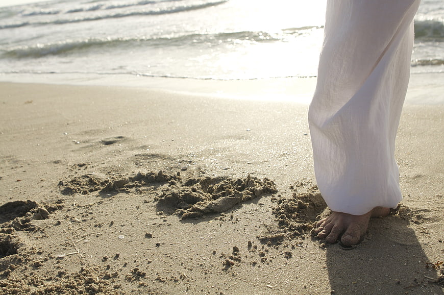Bare feet in sand with white pants on a beach