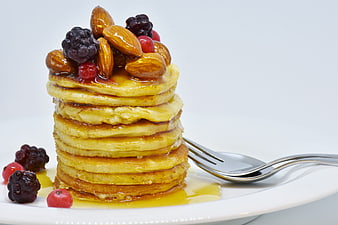 Stack of Pancakes with Honey, Almonds, and Berries on a White Plate