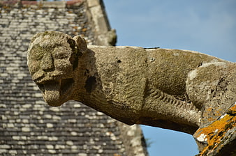 Weathered Stone Gargoyle on Church Roof Against Blue Sky