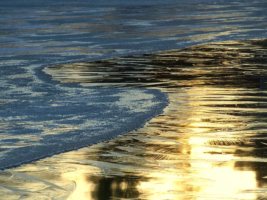 Golden sunlight reflecting on frozen ice and water texture