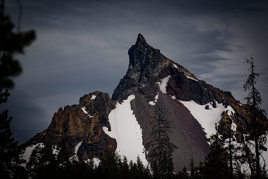 Dramatic Snowy Mountain Peak with Dark Forest Foreground
