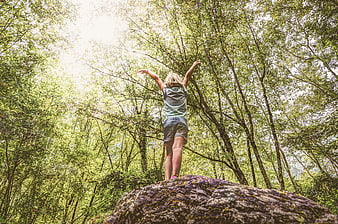 Girl standing on rock raising arms in forest