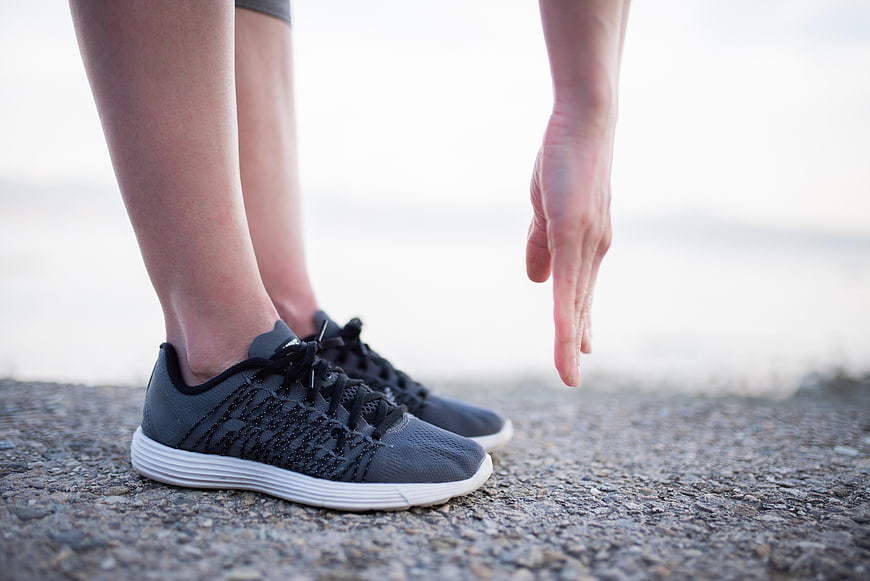 Woman stretching legs in running shoes on asphalt outdoors