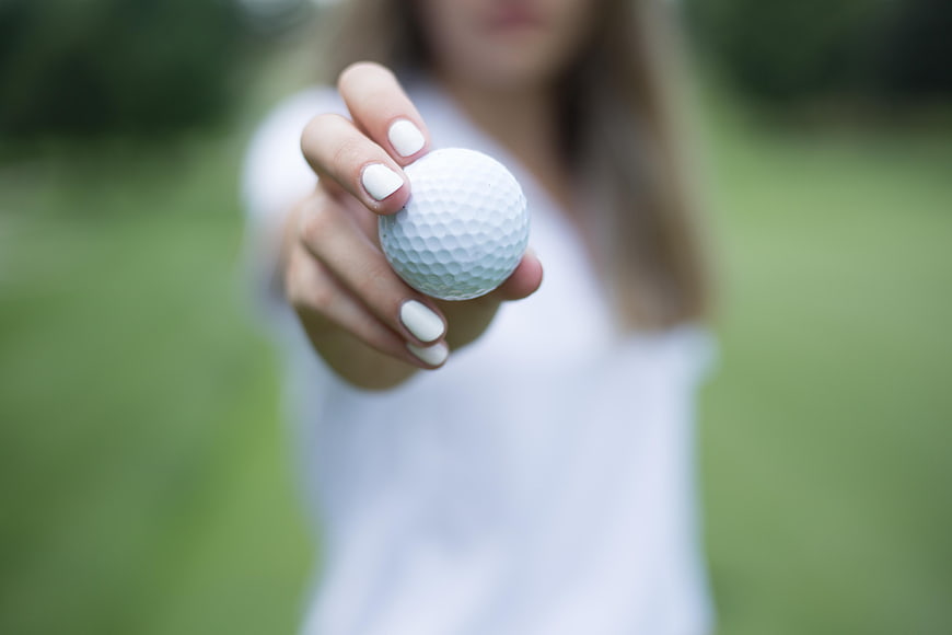 Woman holding golf ball close up on green course