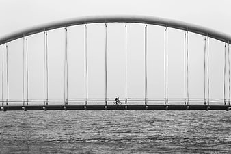 Cyclist Crossing Modern Arch Bridge in Black and White
