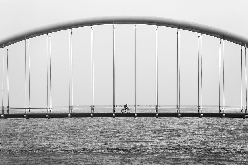 Cyclist Crossing Modern Arch Bridge in Black and White