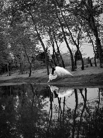 Black and white photo of woman with angel wings sitting by water