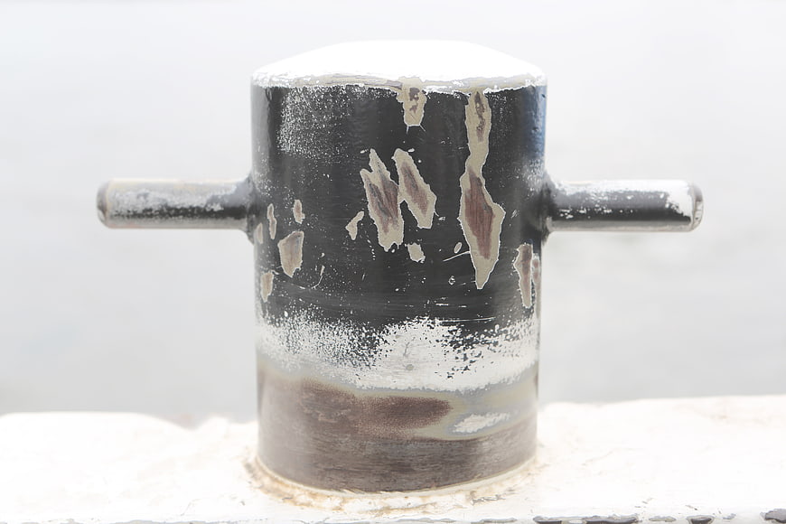 Close-up of weathered black mooring bollard in winter snow