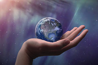 Hand holding a miniature Earth globe against a colorful cosmic nebula background