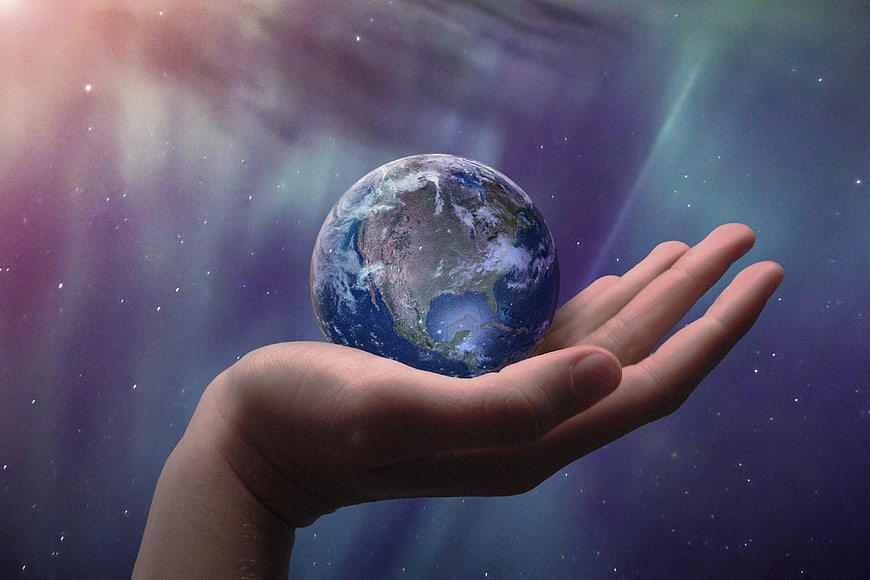 Hand holding a miniature Earth globe against a colorful cosmic nebula background
