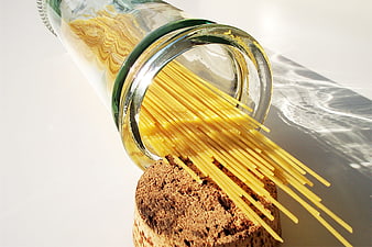 Raw spaghetti noodles spilling from a glass bottle onto a cork stopper