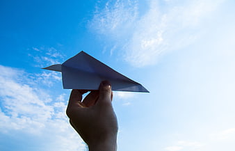Hand holding paper airplane against blue sky
