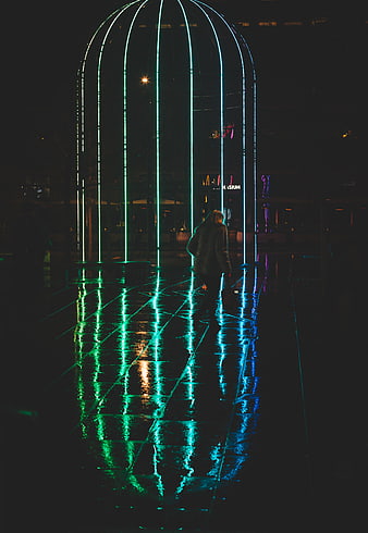 Woman walking under glowing neon arch at night