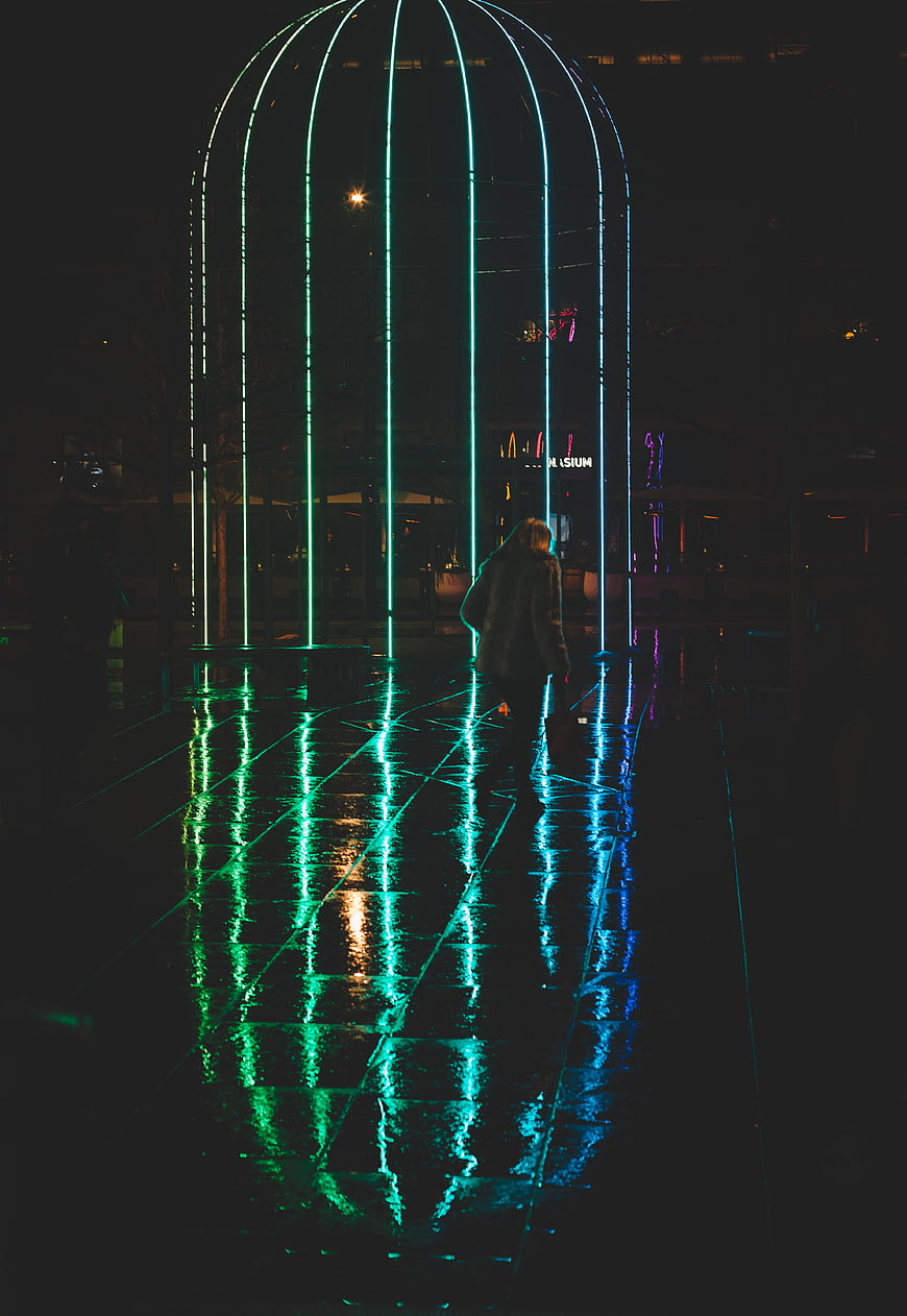 Woman walking under glowing neon arch at night