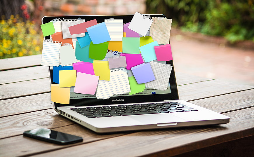 Laptop covered in colorful sticky notes on wooden table