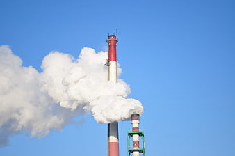 Industrial smokestacks emitting white steam against blue sky