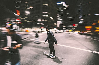 Skateboarder riding through city street at night with motion blur