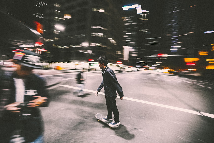 Skateboarder riding through city street at night with motion blur