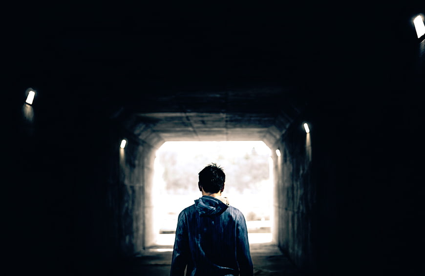 Man Walking Through Dark Tunnel Towards Light