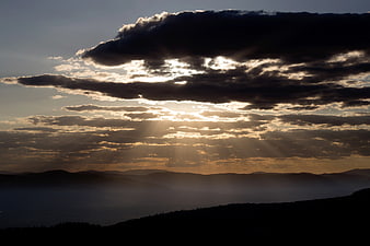 Dramatic Sun Rays Breaking Through Clouds Over Mountain Silhouette