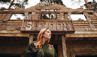 Woman standing in front of rustic wooden saloon sign