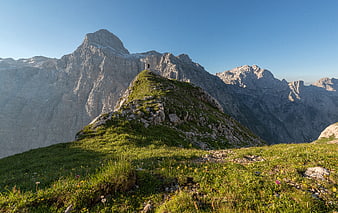 Hiker standing on grassy mountain ridge with rocky peaks
