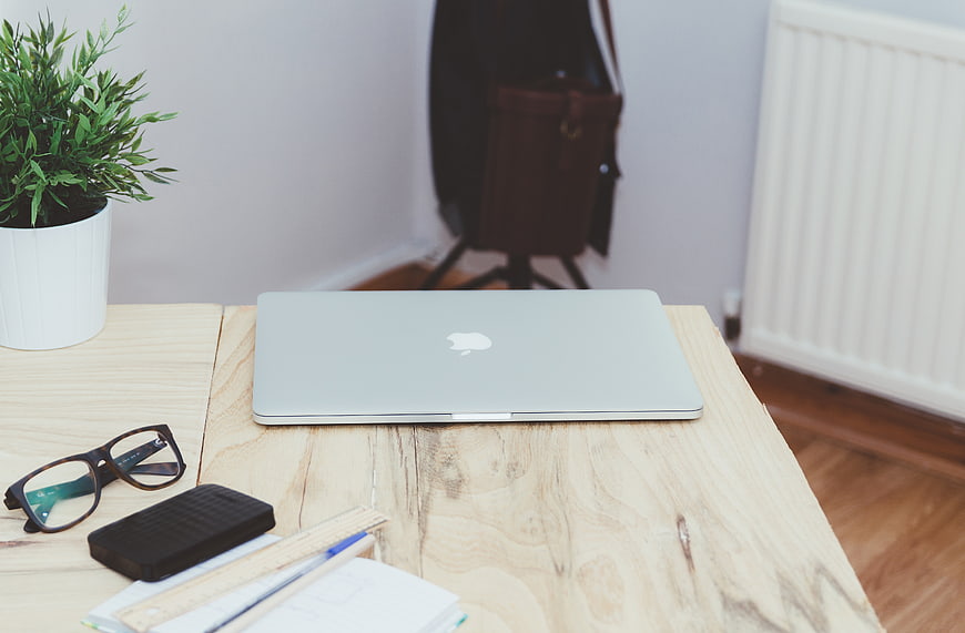 Minimalist wooden desk with laptop, glasses, and notebook