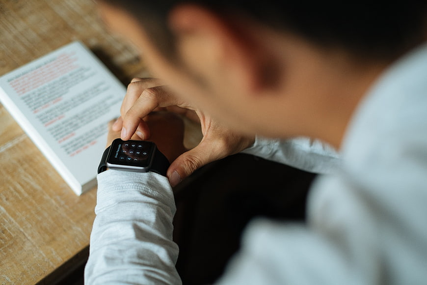 Man Using Smart Watch with Book on Wooden Table