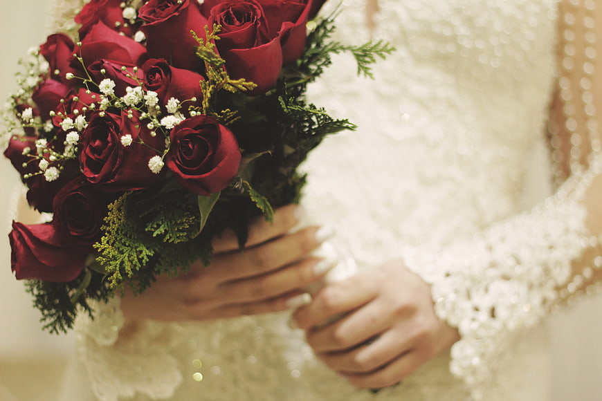Bride holding red rose bouquet in white lace wedding dress