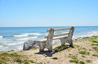 Weathered wooden bench overlooking calm ocean waves on a sunny summer day