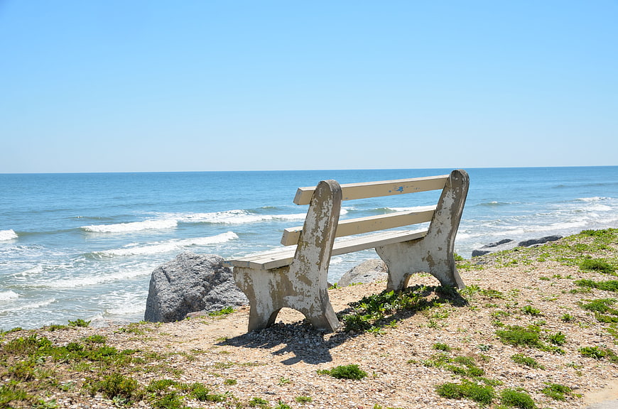 Weathered wooden bench overlooking calm ocean waves on a sunny summer day