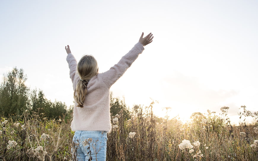 Woman with arms raised in field at sunset