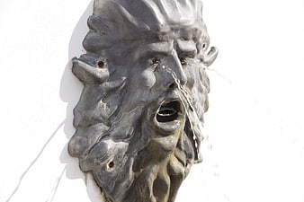 Bronze face fountain sculpture on white wall