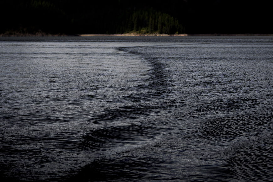 Dark moody ocean waves with distant forest shoreline